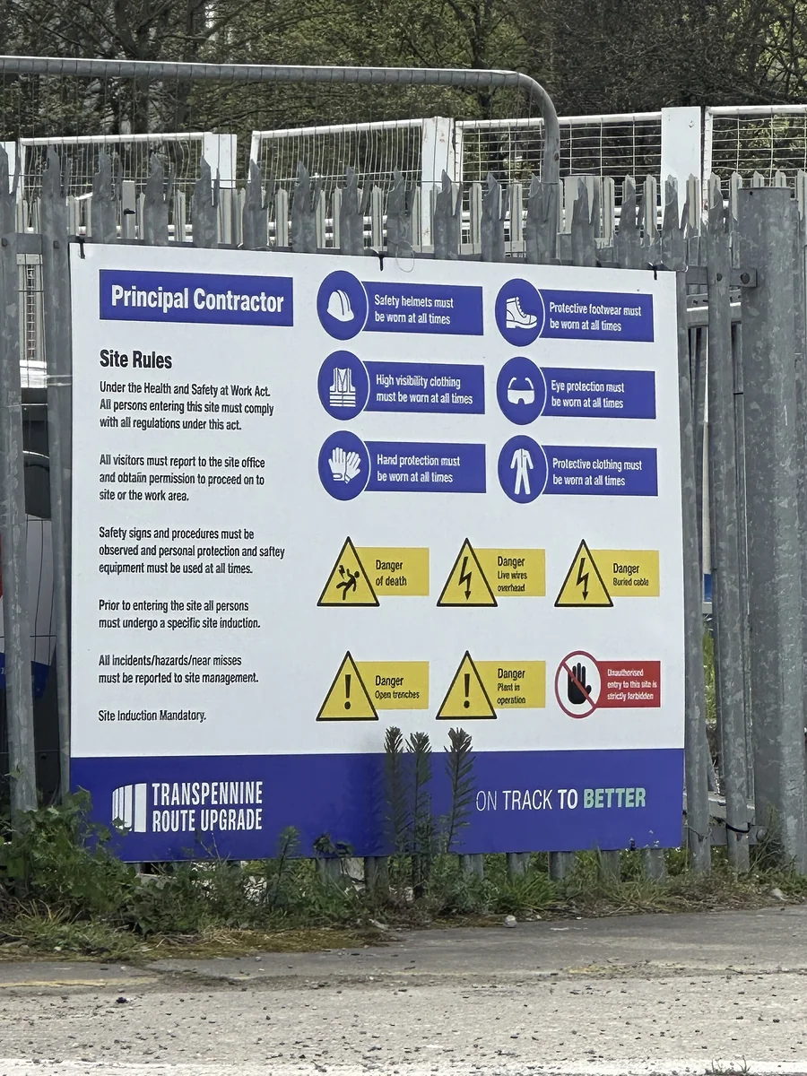 Bord met veiligheidsregels en verplichte beschermingsmiddelen aan een bouwhek
