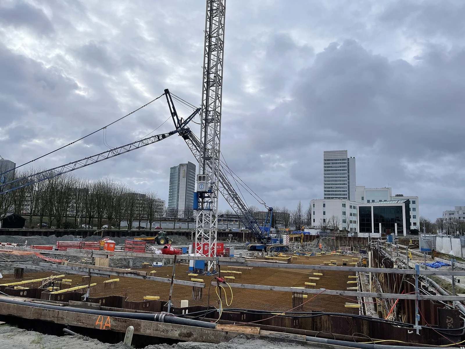 Bouwplaats met torenkraan, bouwput en bekisting onder een bewolkte lucht